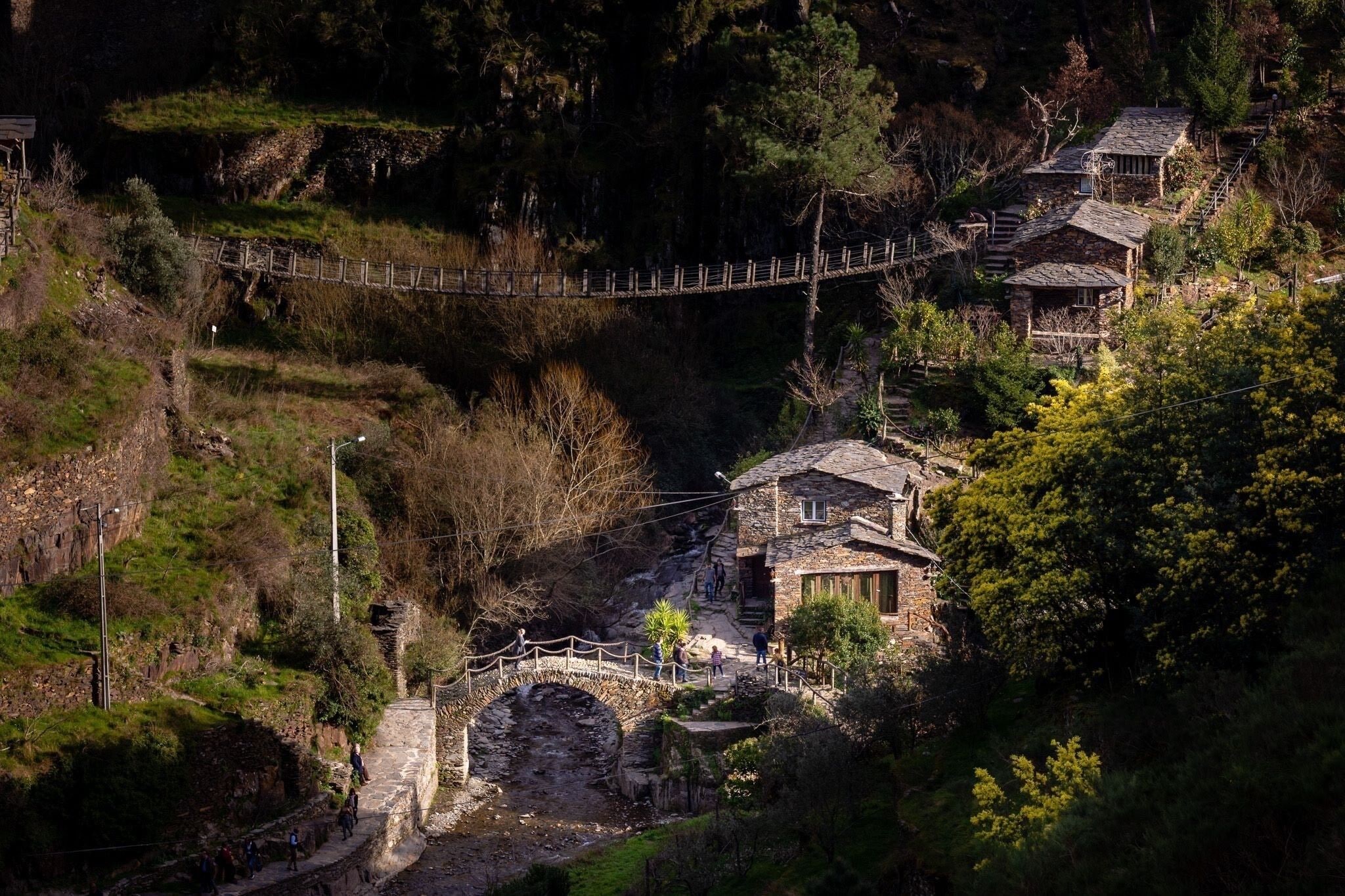 A stone bridge, a wooden footbridge, and traditional houses on a hillside.