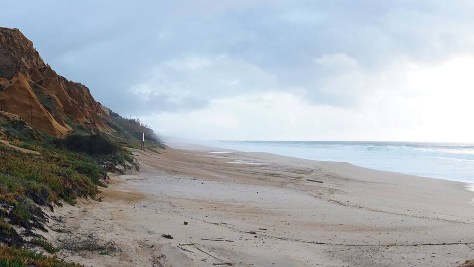 A coastal landscape with a sandy beach, rocky cliffs, and ocean waves.