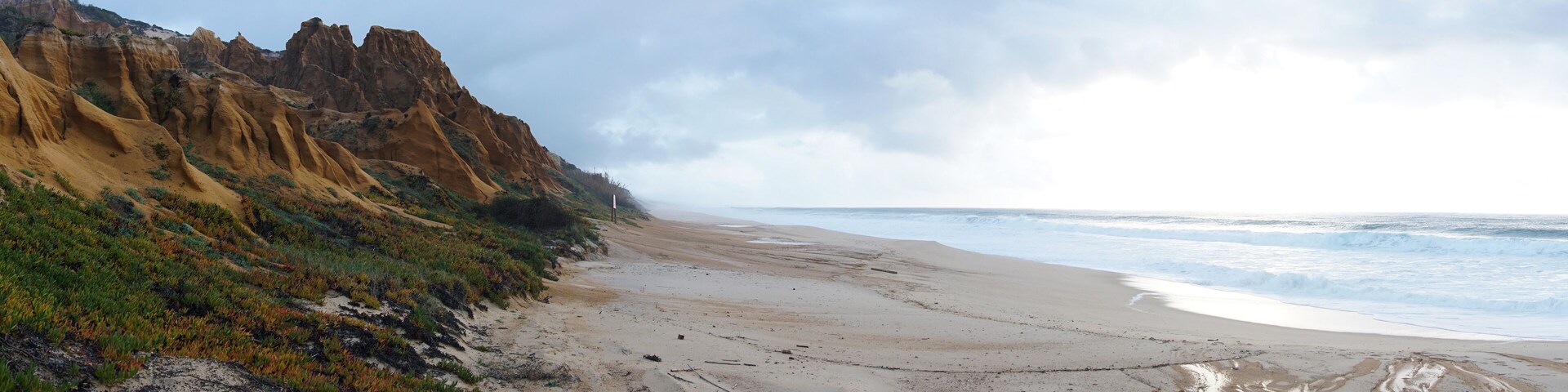 Un paisaje costero con una playa arenosa, acantilados rocosos y olas del océano.