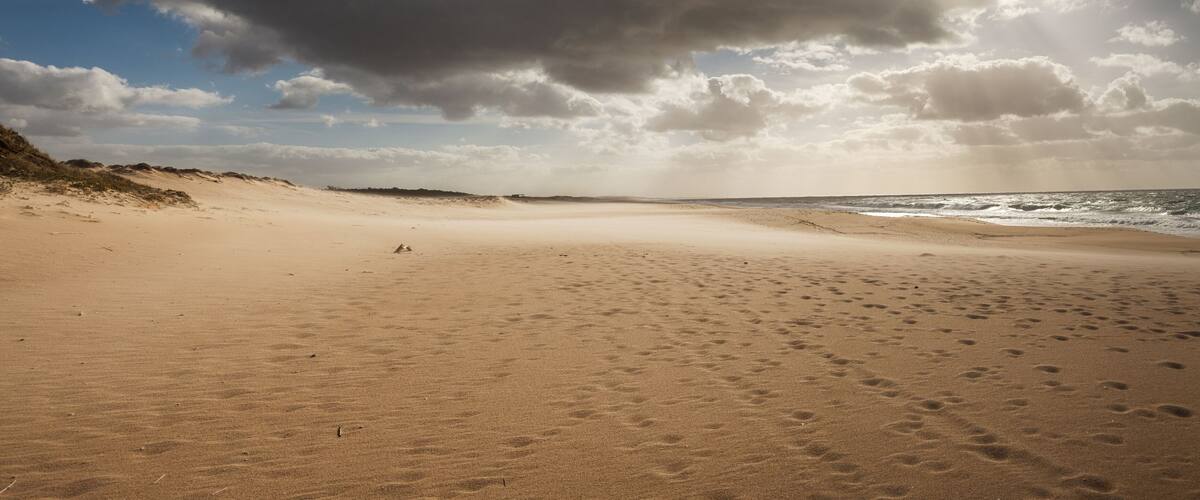 Ein Sandstrand mit Fußabdrücken und einer Düne links.
