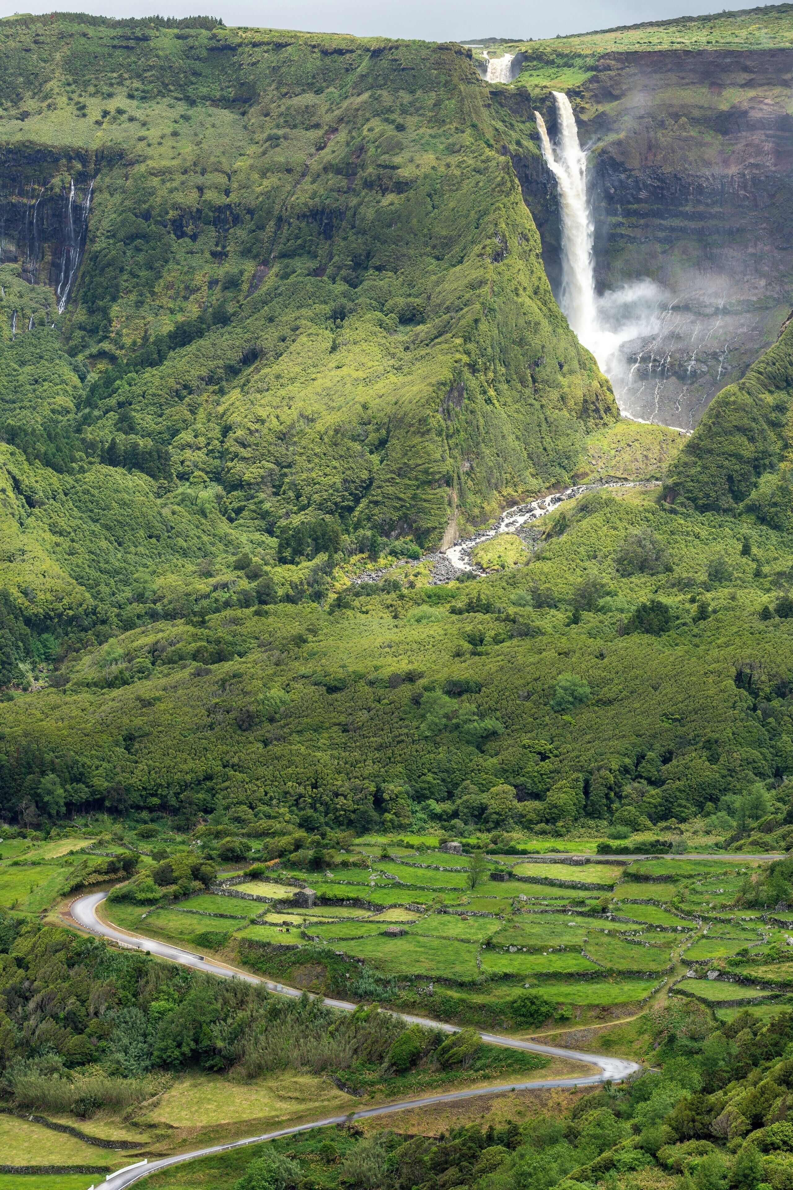 A lush valley with a waterfall and terraced fields.