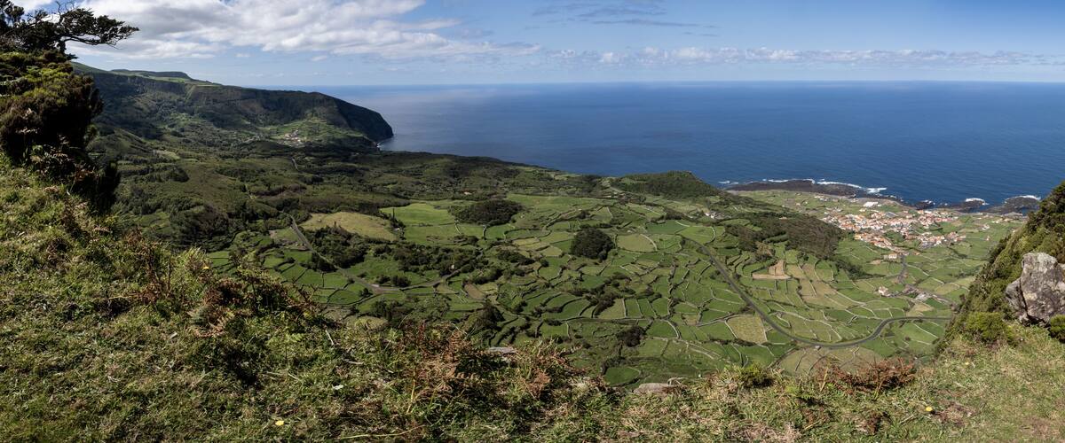 A coastal landscape with terraced fields, a village, and a cliff overlooking the sea.