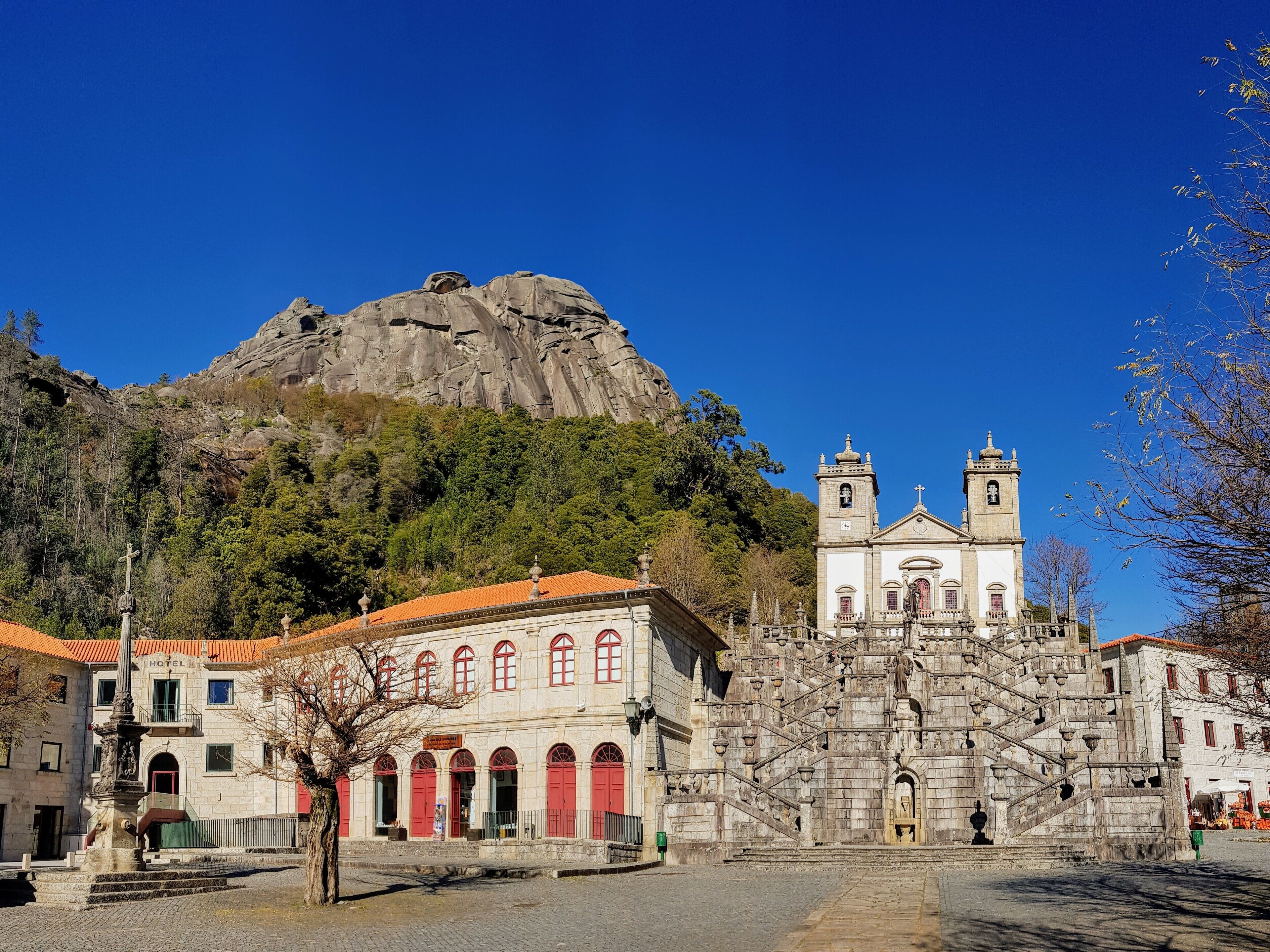 A historic church with a bell tower, a mountain in the background, and a hotel in the foreground.