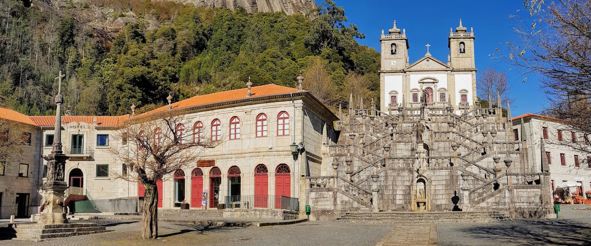 A historic church with a bell tower, a mountain in the background, and a hotel in the foreground.