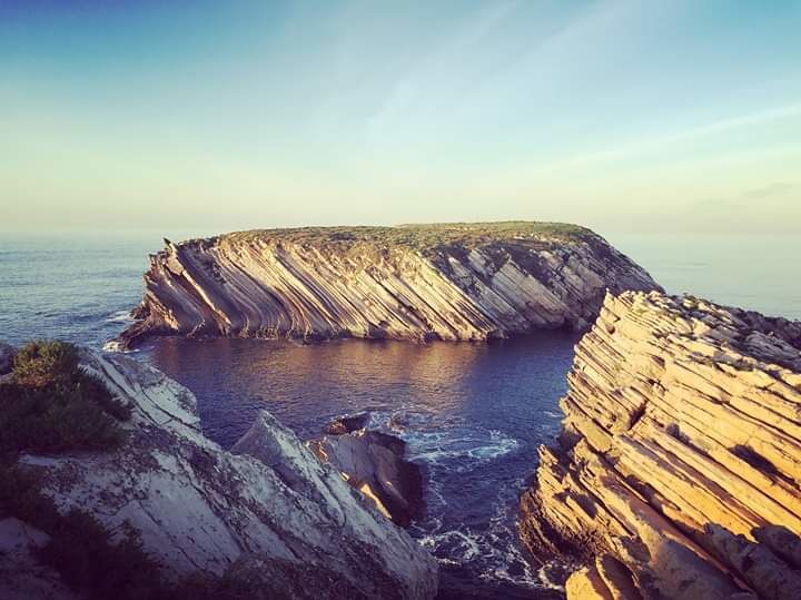A coastal cliff formation with stratified rock layers and a body of water at its base.