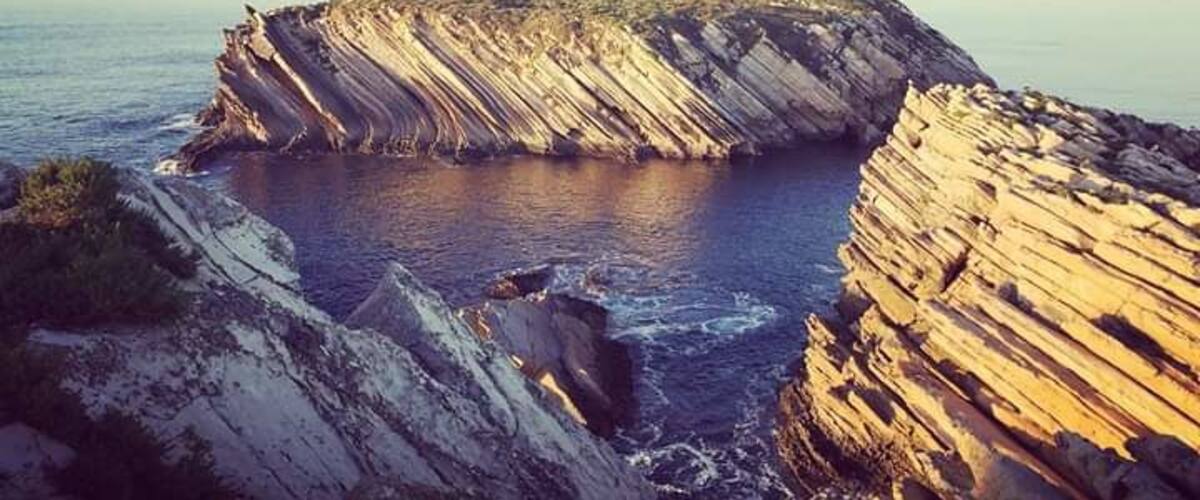 A coastal cliff formation with stratified rock layers and a body of water at its base.