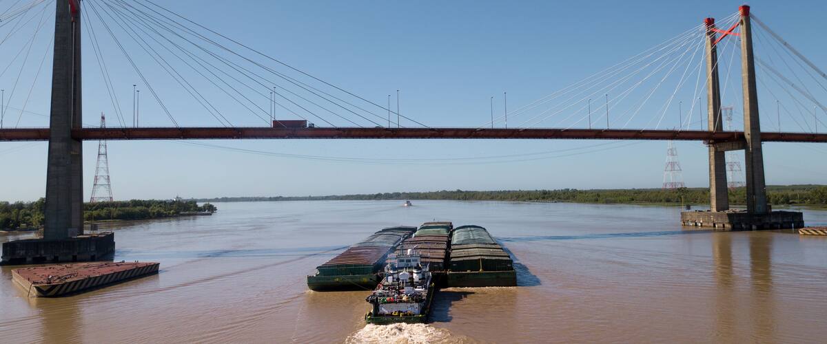 A large bridge spanning a river with a cargo ship passing underneath.