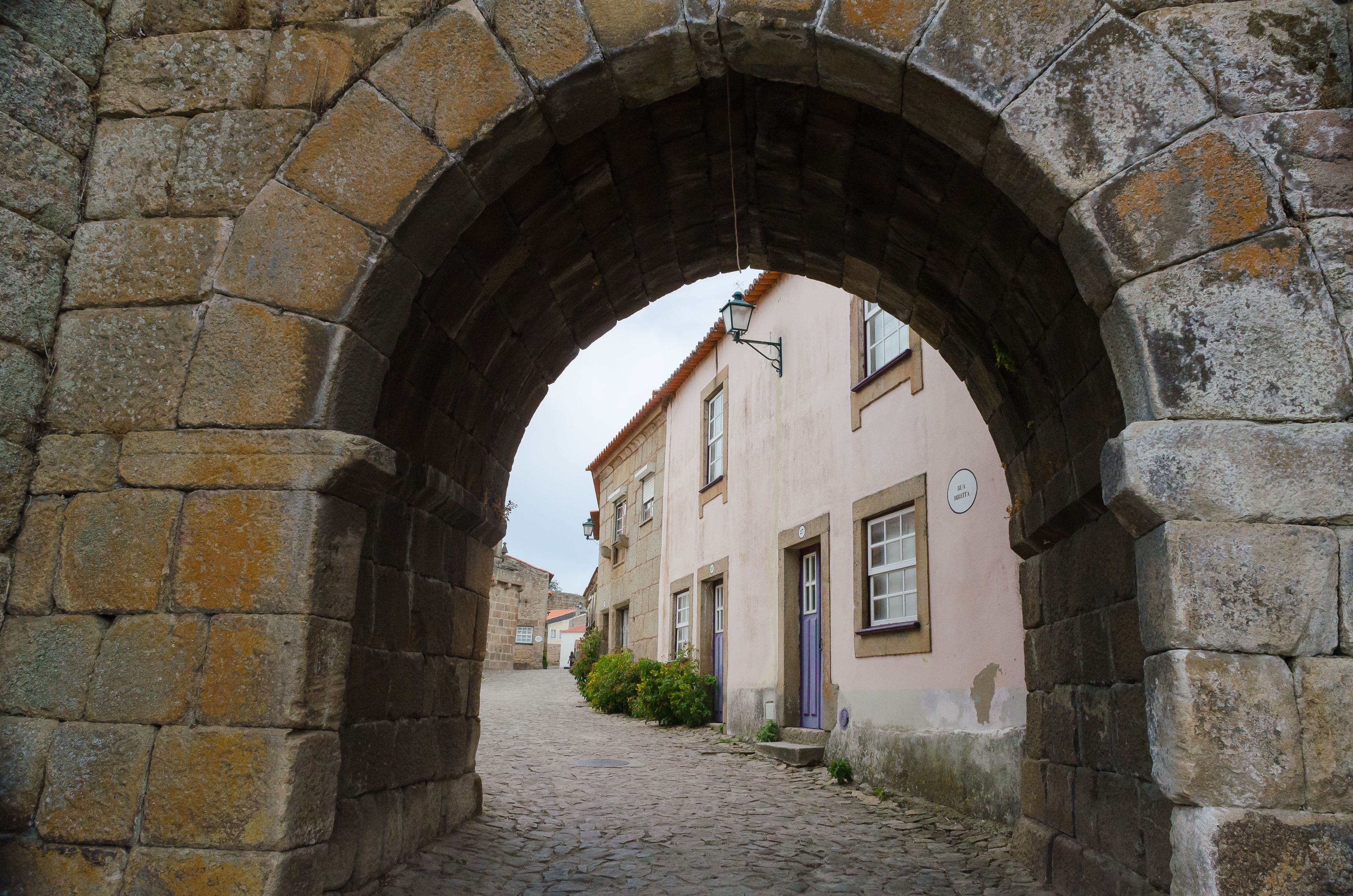 Un antiguo arco de piedra que da acceso a una calle adoquinada bordeada de edificios.