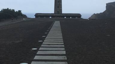 A lighthouse with a spiral staircase leading up to it, set against a cloudy sky.