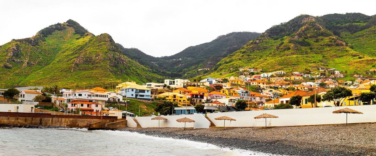 A coastal town with colorful buildings, a rocky beach, and green mountains in the background.