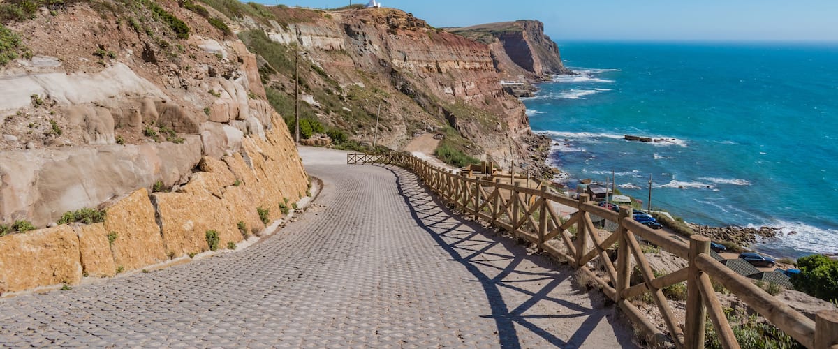 Sidewalk on cliffs with wooden fence and turquoise sea on the horizon at Assenta beach, Ericeira - Mafra PORTUGAL