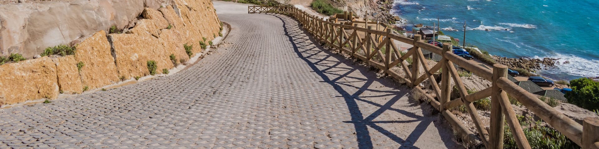 Sidewalk on cliffs with wooden fence and turquoise sea on the horizon at Assenta beach, Ericeira - Mafra PORTUGAL