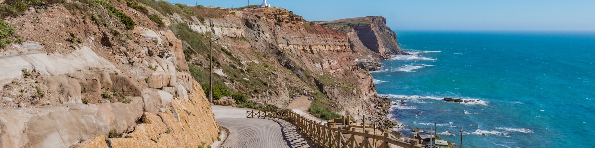Sidewalk on cliffs with wooden fence and turquoise sea on the horizon at Assenta beach, Ericeira - Mafra PORTUGAL