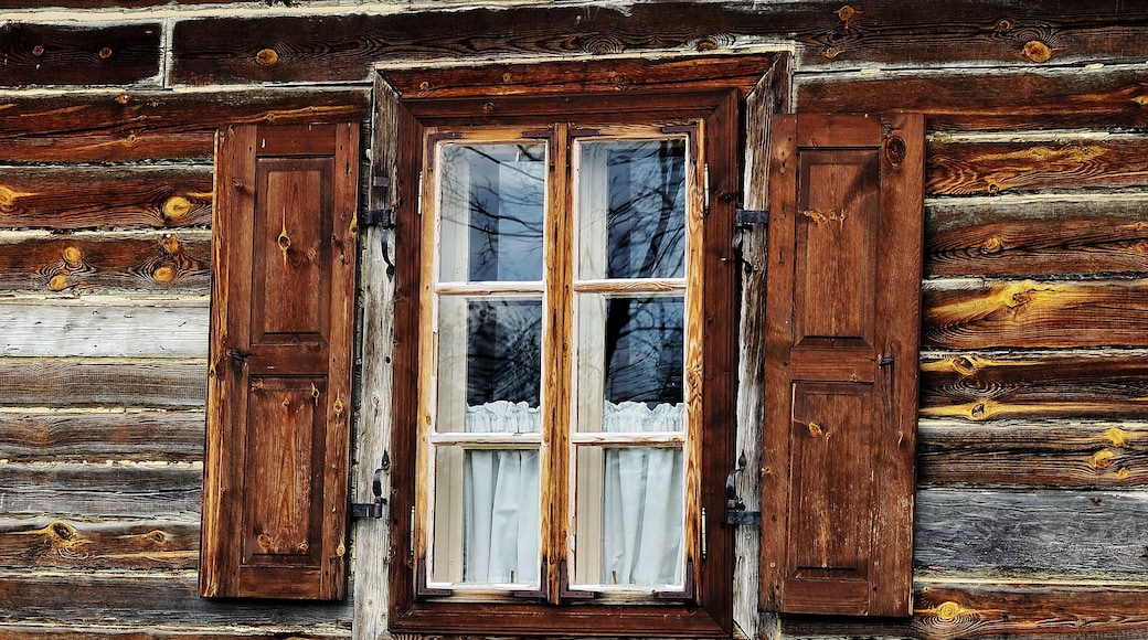 A rustic wooden cabin with a window featuring two wooden shutters and a white curtain.