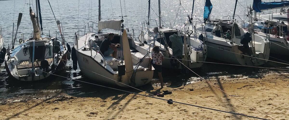Sailboats docked on a sandy beach with a forested island in the background.