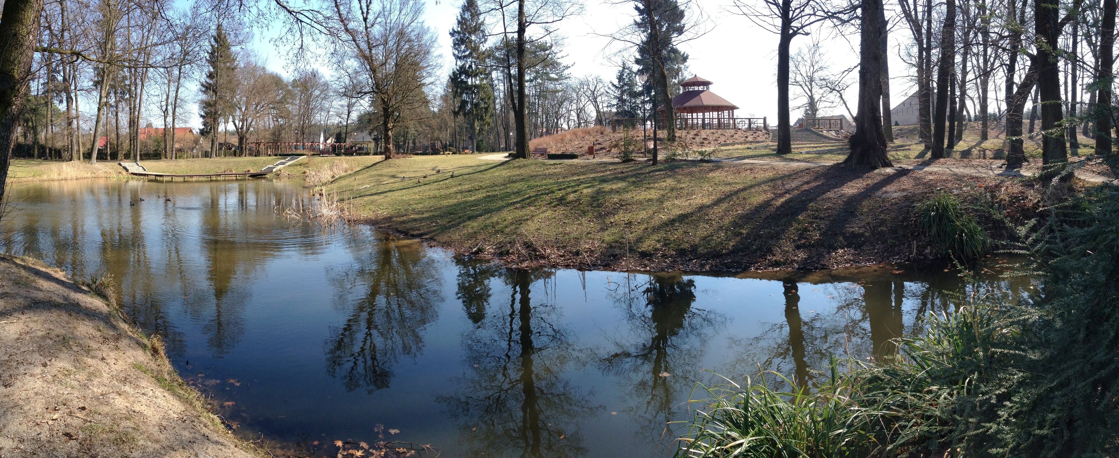 A pond surrounded by trees, a gazebo, and a small bridge.