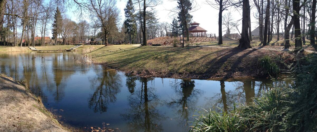 A pond surrounded by trees, a gazebo, and a small bridge.