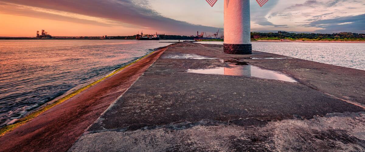 A windmill by a waterfront with a sunset in the background.