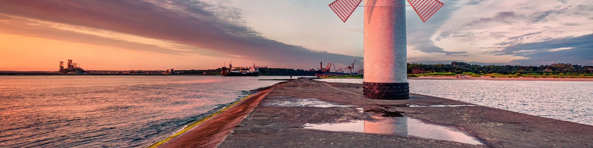 A windmill by a waterfront with a sunset in the background.