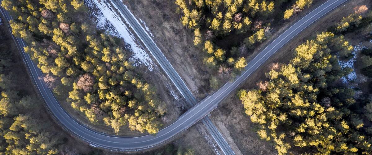 An aerial view of a winding road through a forest with yellow foliage.