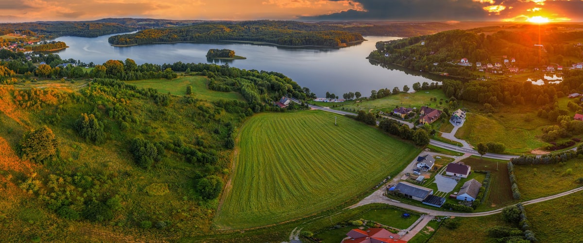 Un lago rodeado de colinas boscosas, un pequeño pueblo y un atardecer.