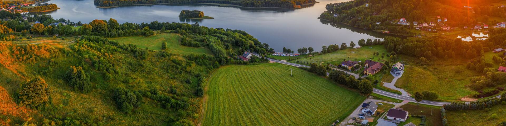 A lake surrounded by forested hills, a small village, and a sunset.