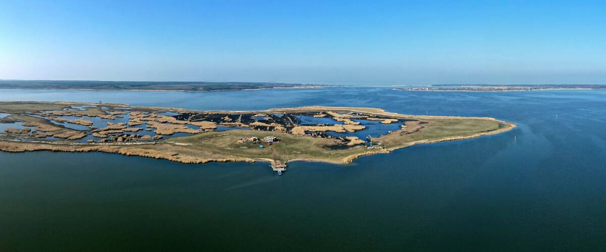 An aerial view of a small island with a lighthouse, surrounded by calm waters and distant land.