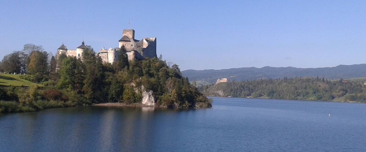 A castle on a hill overlooking a calm lake.