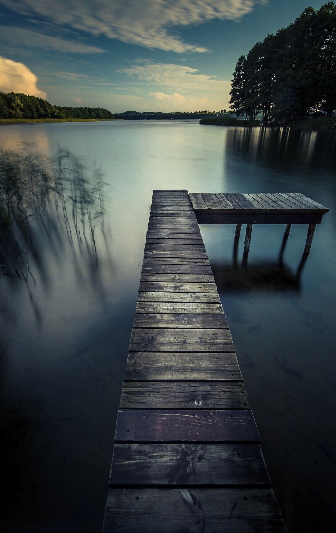 A wooden pier extending into calm water with a clear sky above.