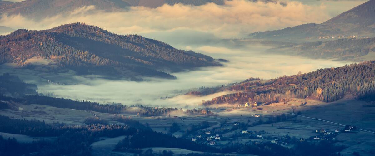 A mountainous landscape with rolling hills, a valley, and a village nestled among the trees.