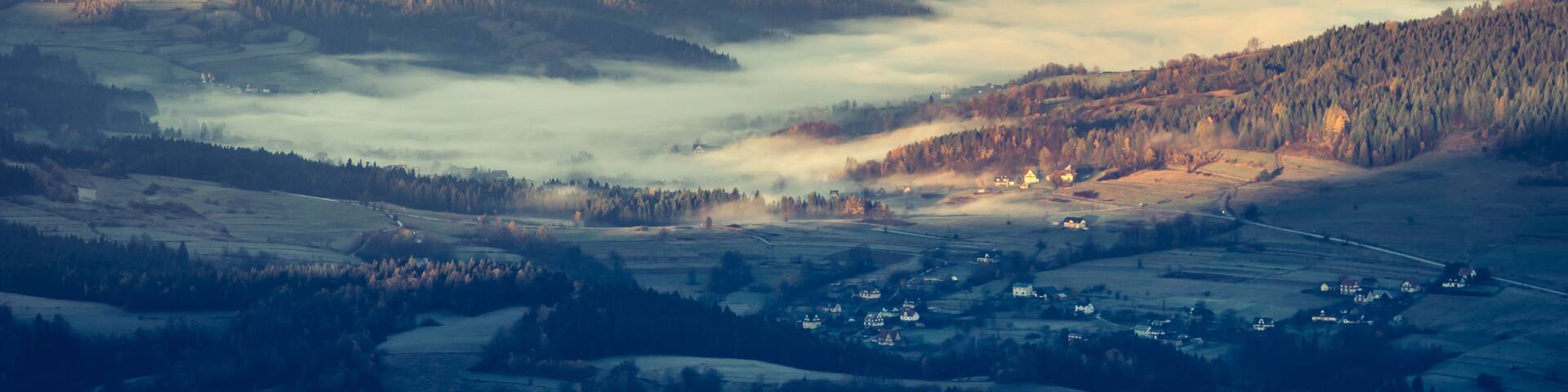 A mountainous landscape with rolling hills, a valley, and a village nestled among the trees.