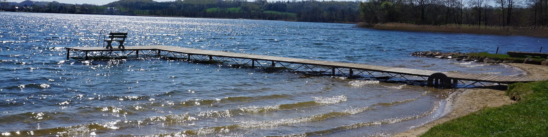 A wooden pier extending into a lake with a bench at the end.