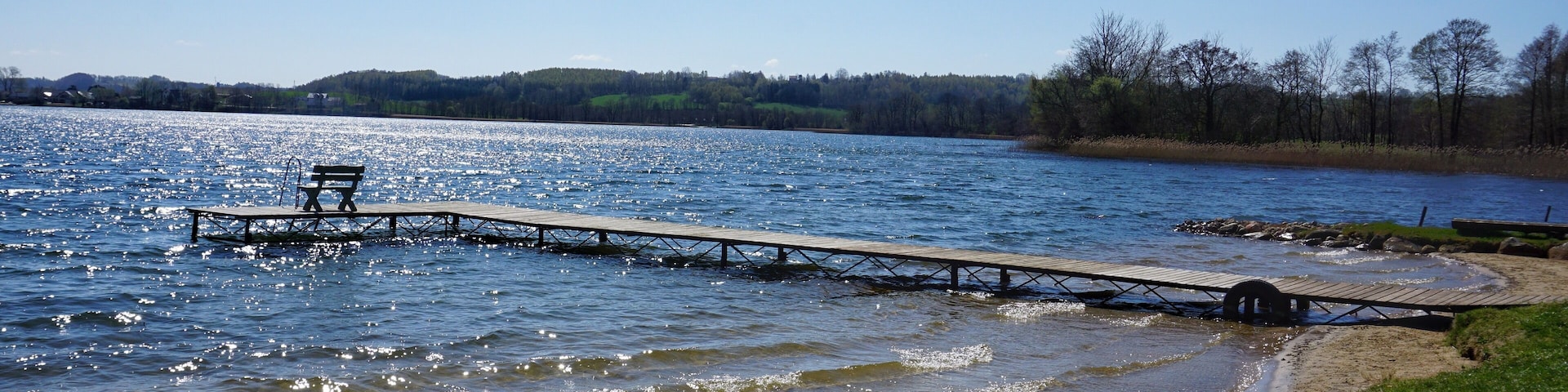 Un muelle de madera que se adentra en un lago, con un banco al final.