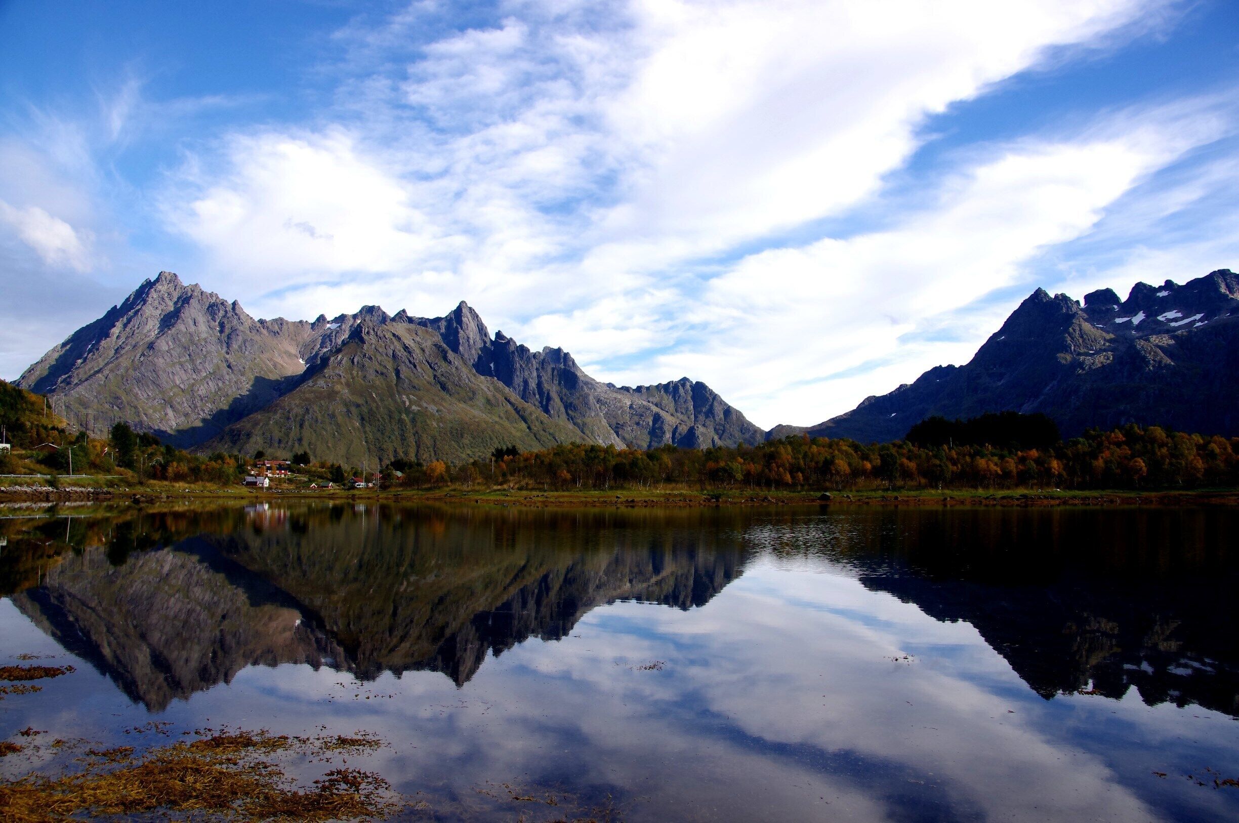 A mountain range reflected in a calm lake with a clear sky.