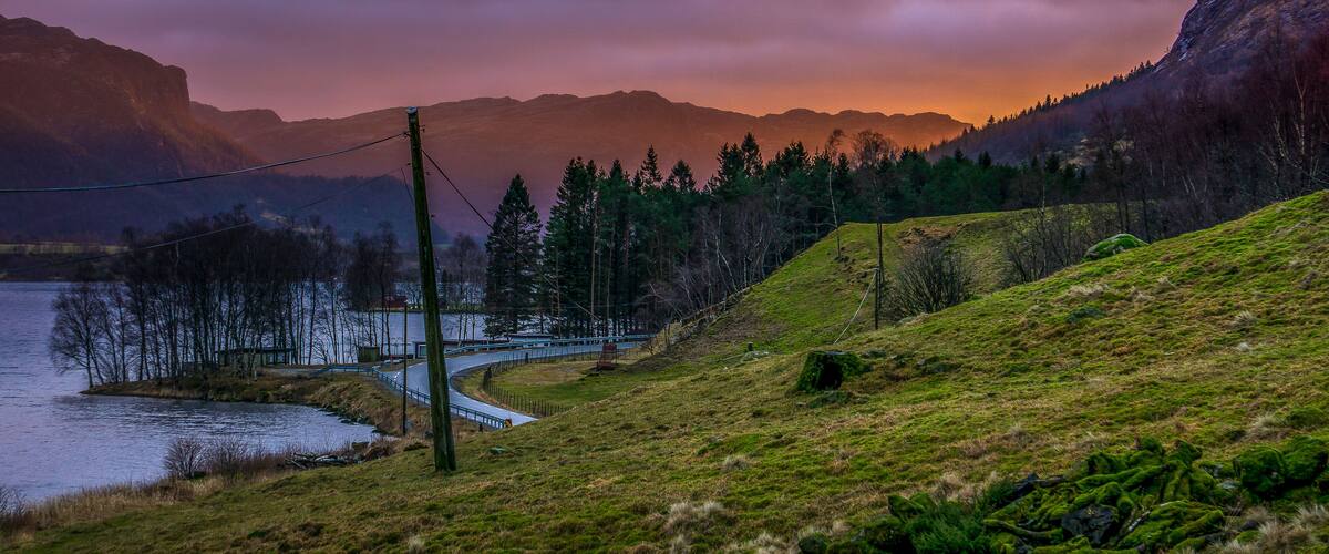 A winding road beside a lake with mountains in the background.