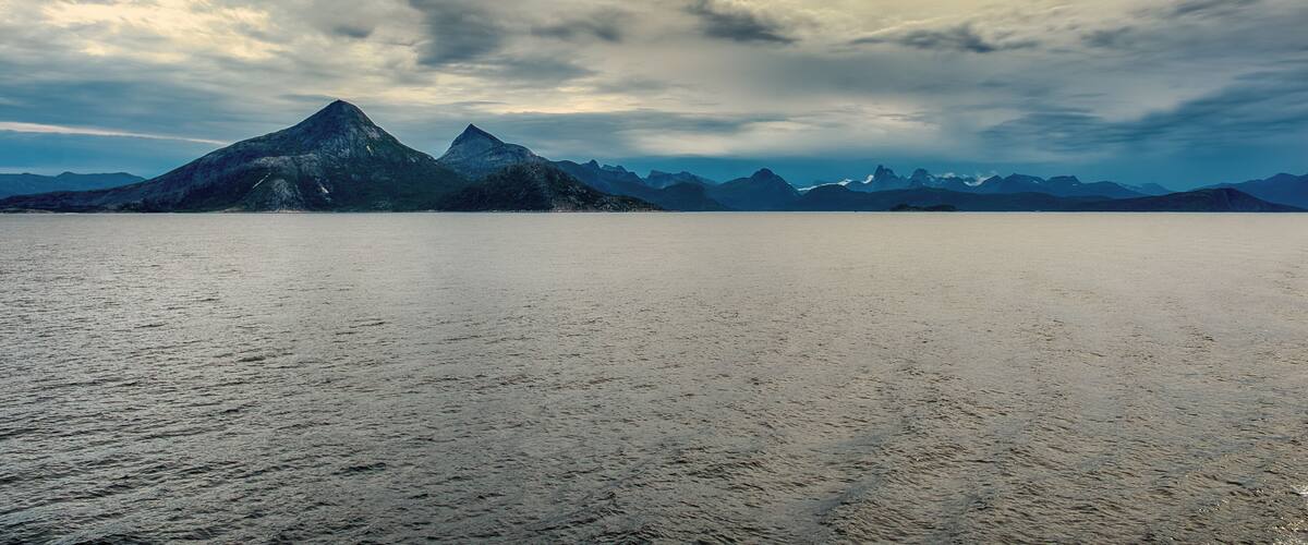 A calm lake with mountains in the background under a cloudy sky.