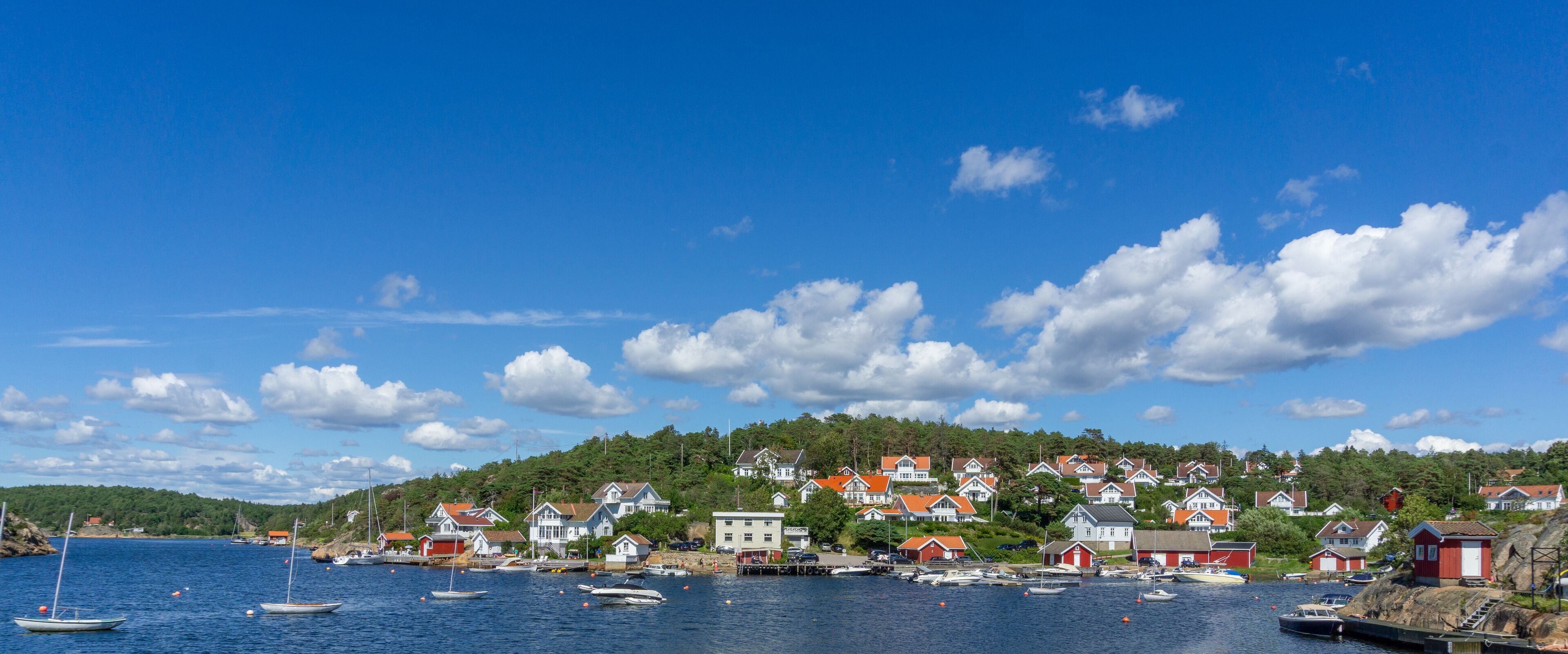 A coastal village with houses on a hillside, boats in the water, and a clear blue sky.