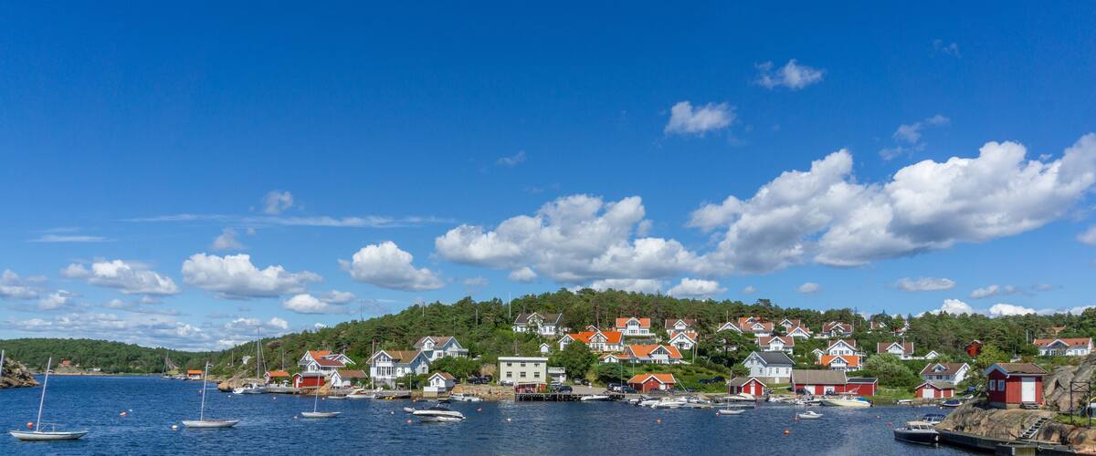 A coastal village with houses on a hillside, boats in the water, and a clear blue sky.