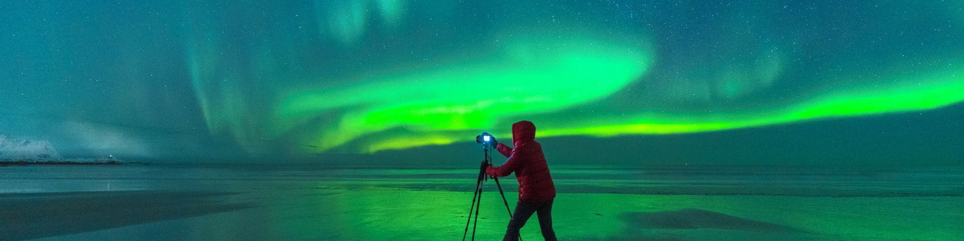 Una persona con cámara sobre trípode, capturando las auroras boreales sobre un paisaje helado.