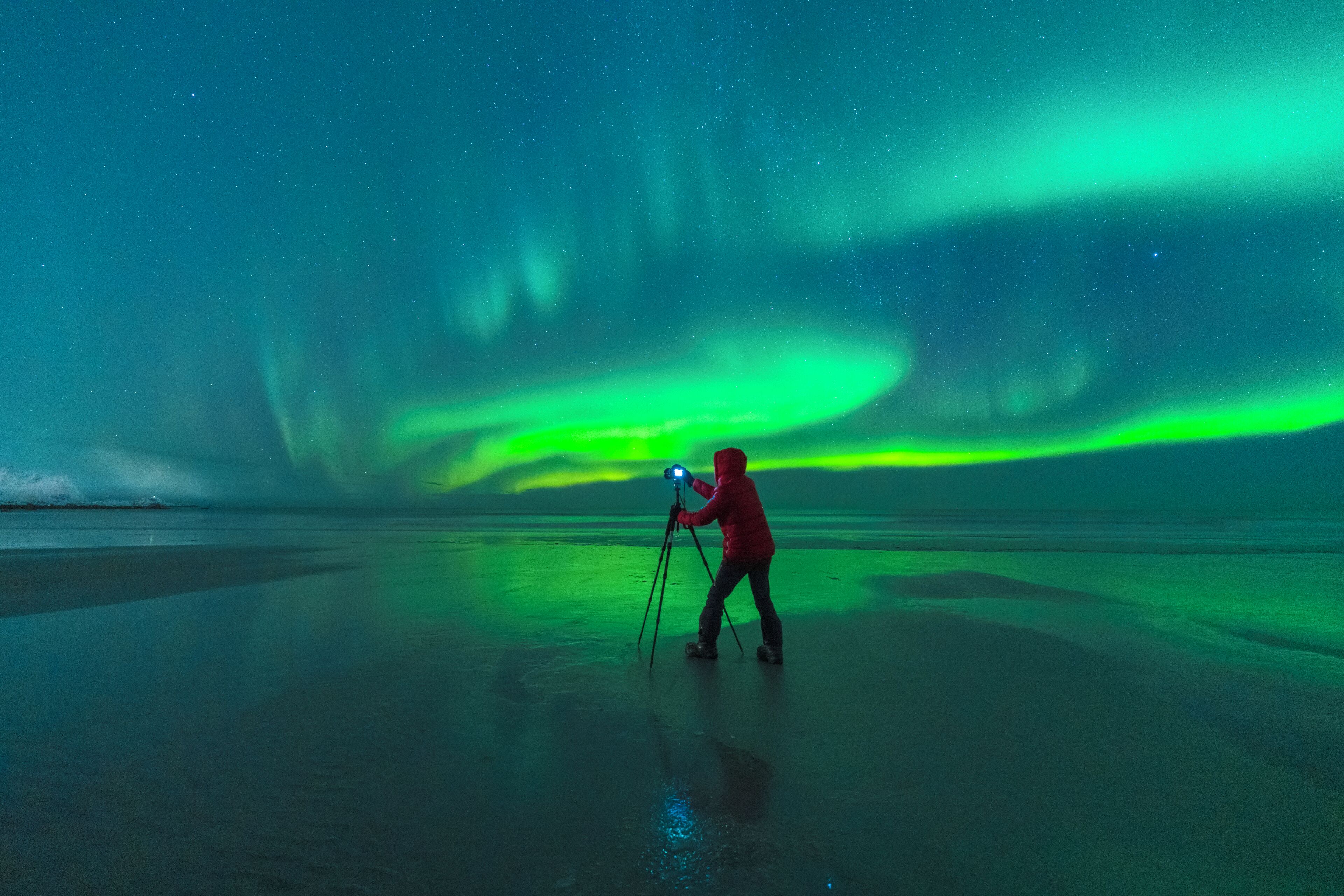 A person with a camera on a tripod, capturing the Northern Lights over a frozen landscape.