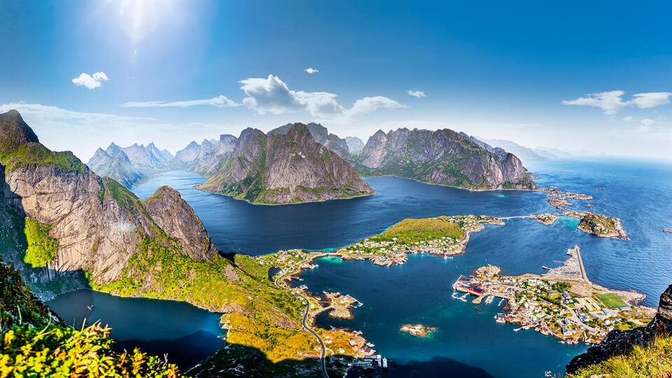 A coastal landscape with rugged mountains, a bay with clear waters, and a small town with visible buildings and docks.