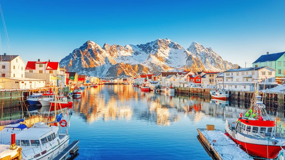 A harbor with boats, buildings, and snow-covered mountains in the background.