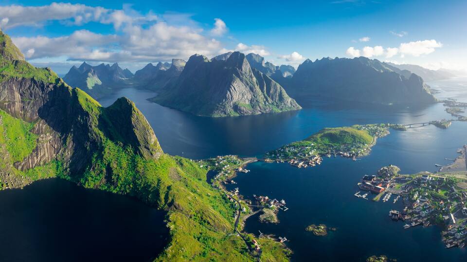 A mountainous landscape with a fjord, a small town, and a bridge connecting the land to the water.