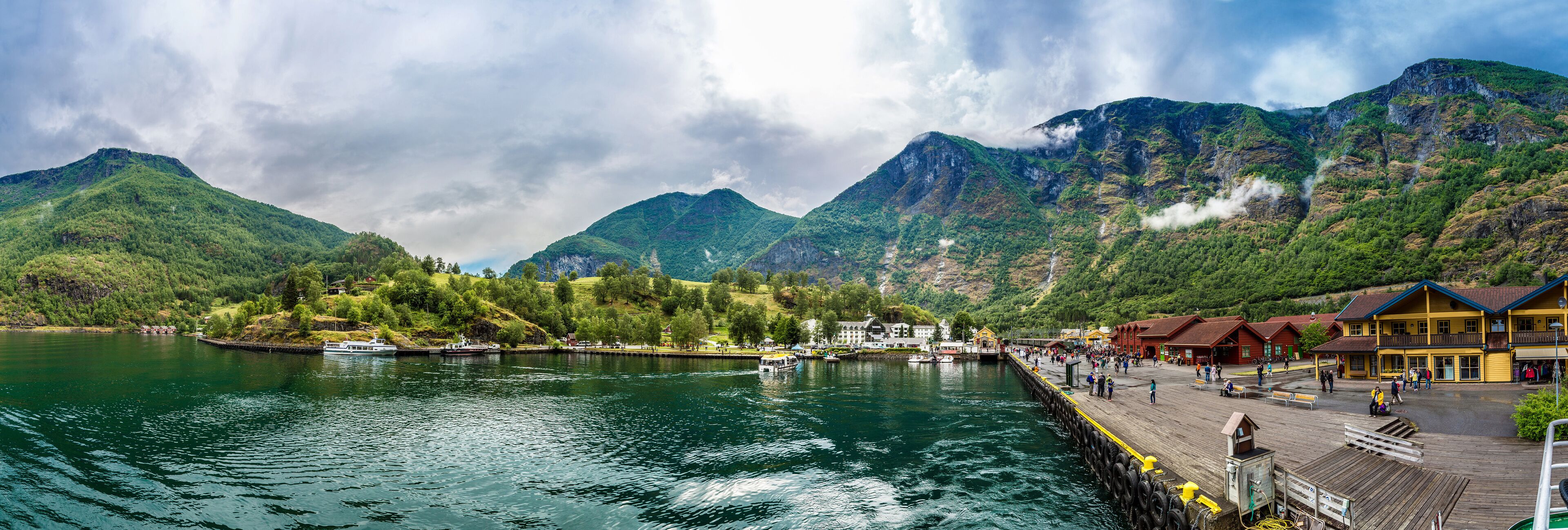 A lake with boats, a wooden pier, and buildings in the background.