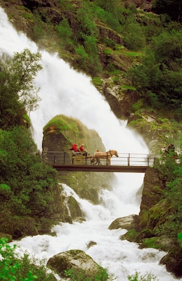 Tourist crossing a waterfall on a bridge with a horse cart, Olden, Norway