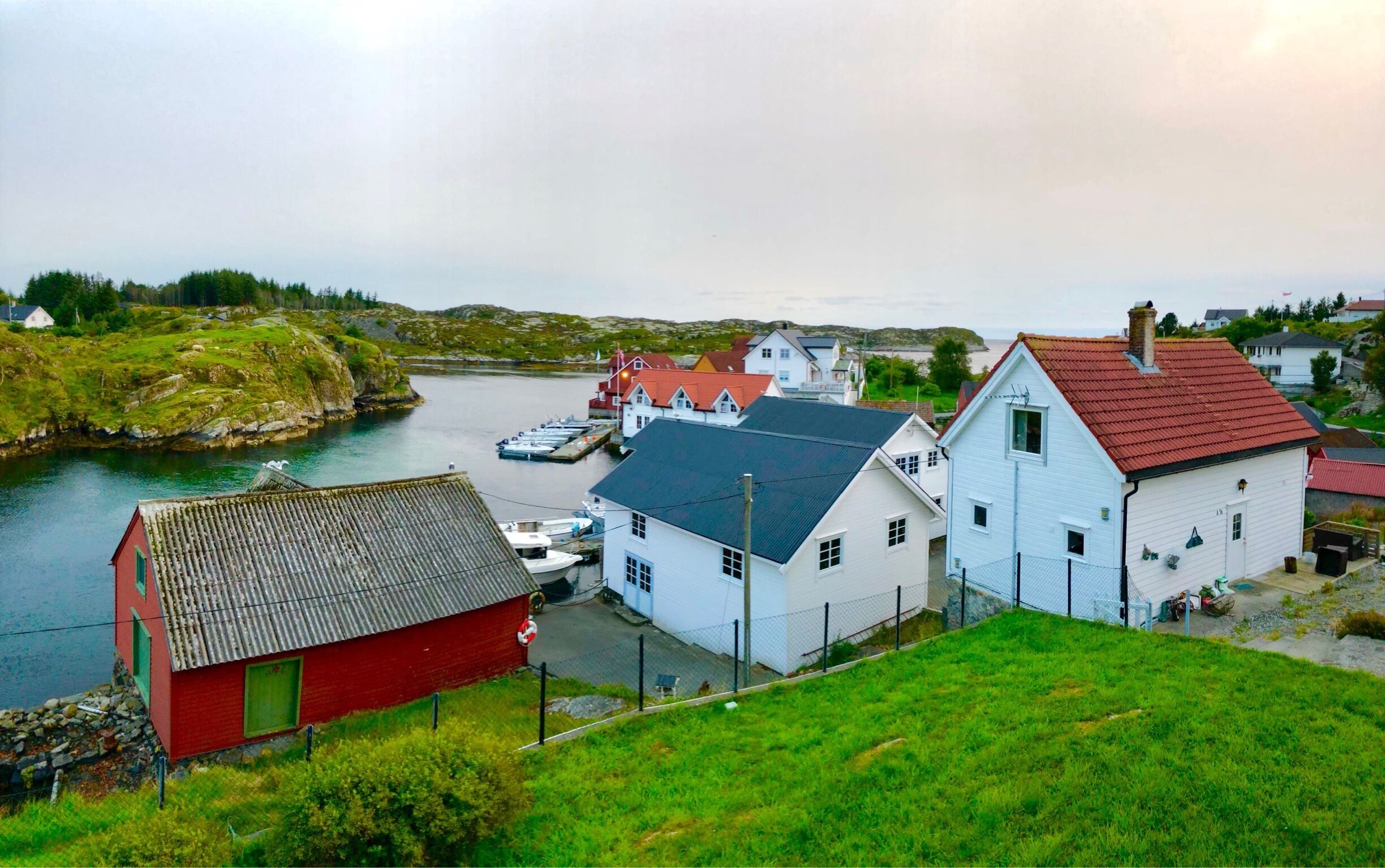 A coastal village with houses by the water, a dock with boats, and a red building.
