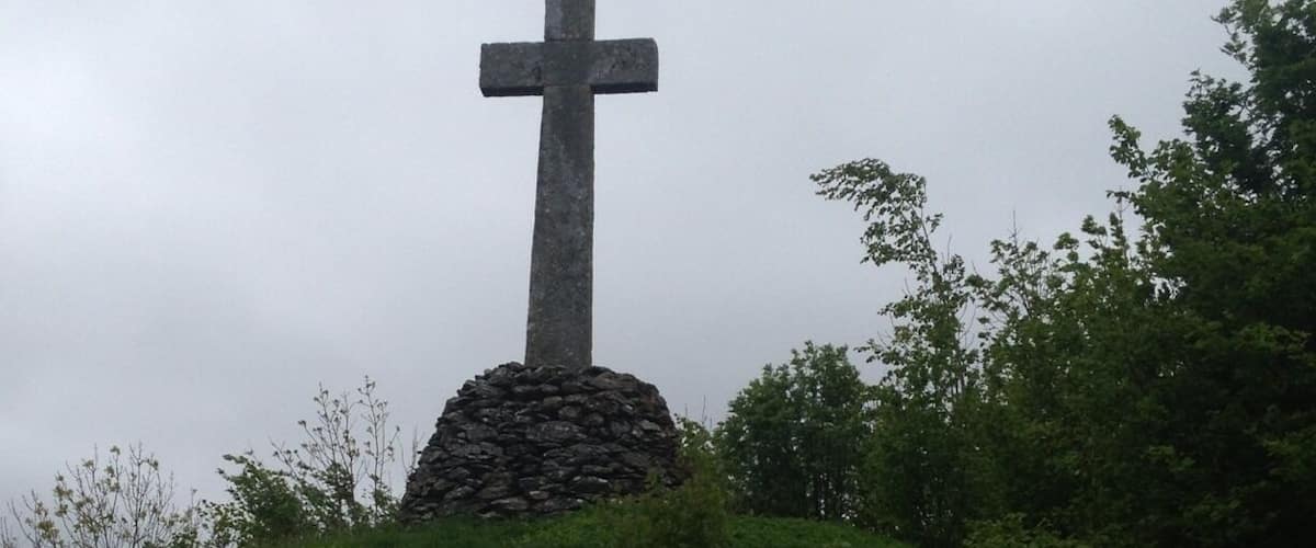 A stone cross on a hill with surrounding greenery.