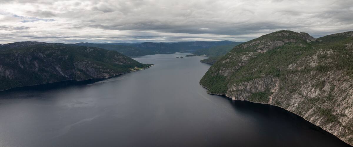 A large lake surrounded by forested mountains under a cloudy sky.