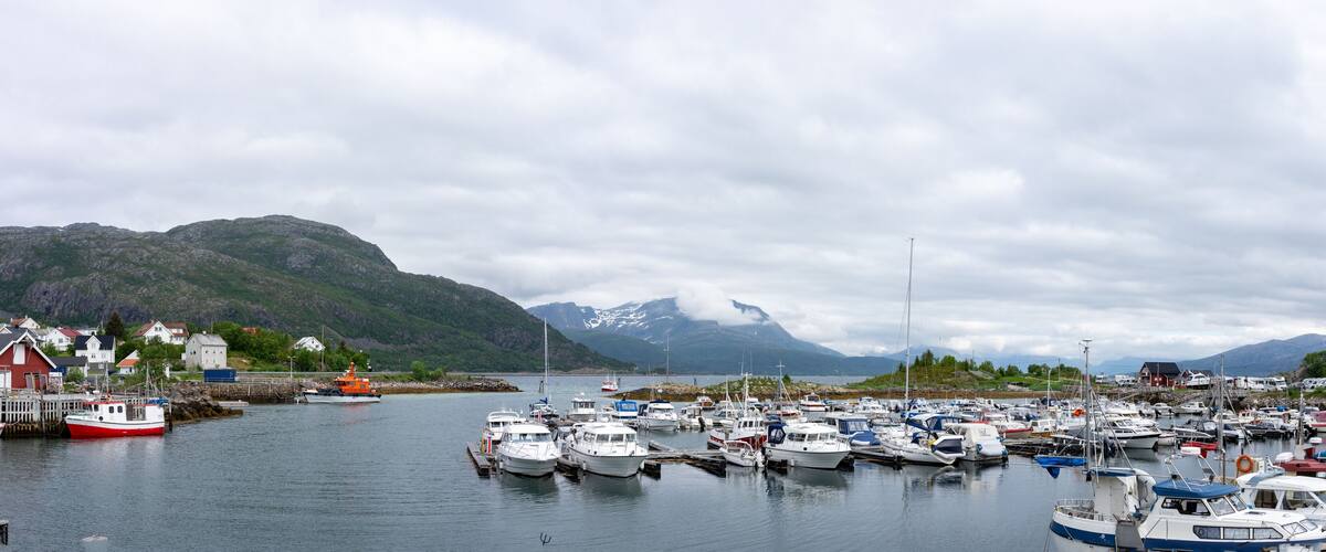 A harbor with numerous boats, a lighthouse, and mountains in the background.