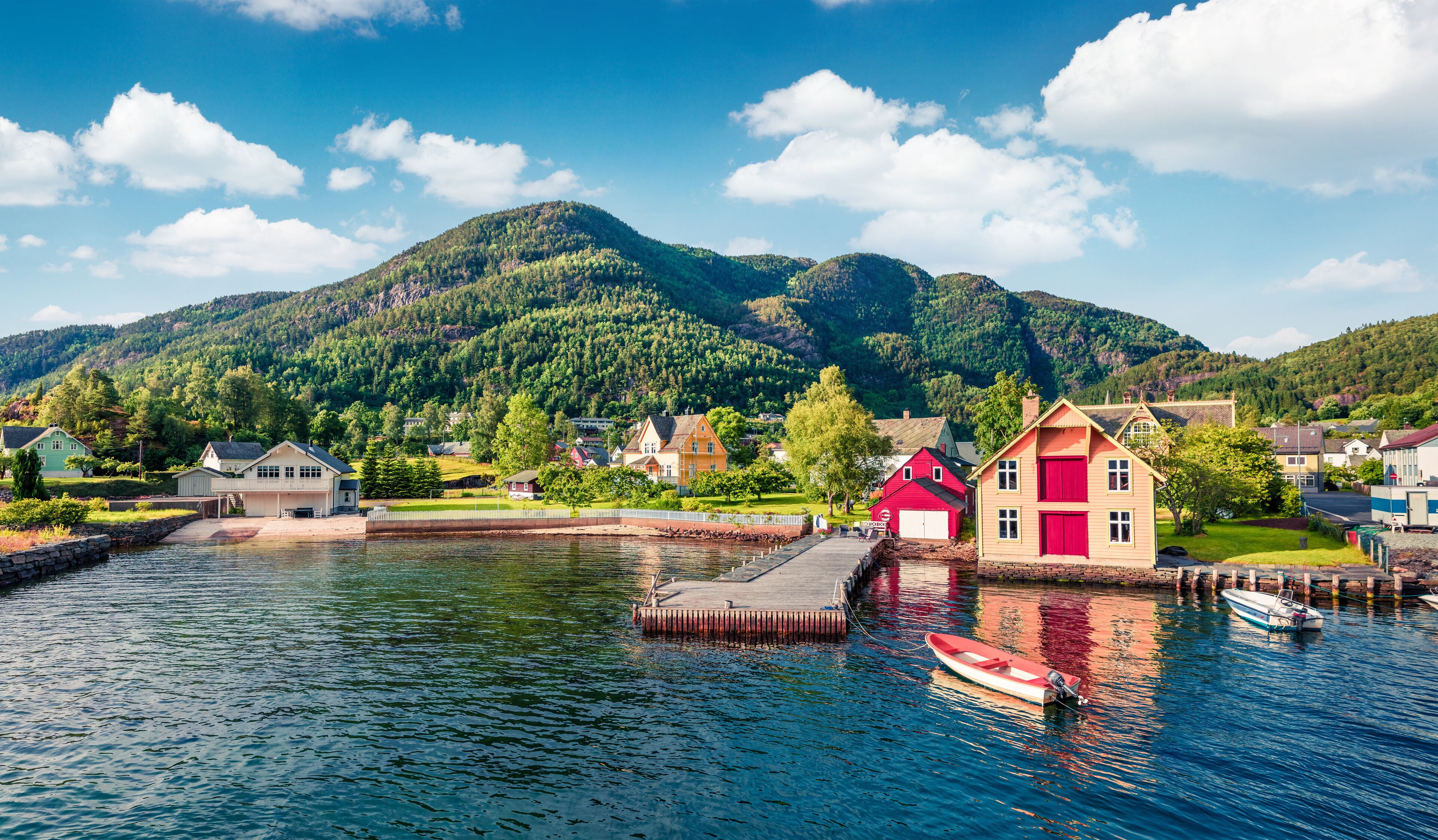 A lakeside village with houses, a dock, and a mountain in the background.